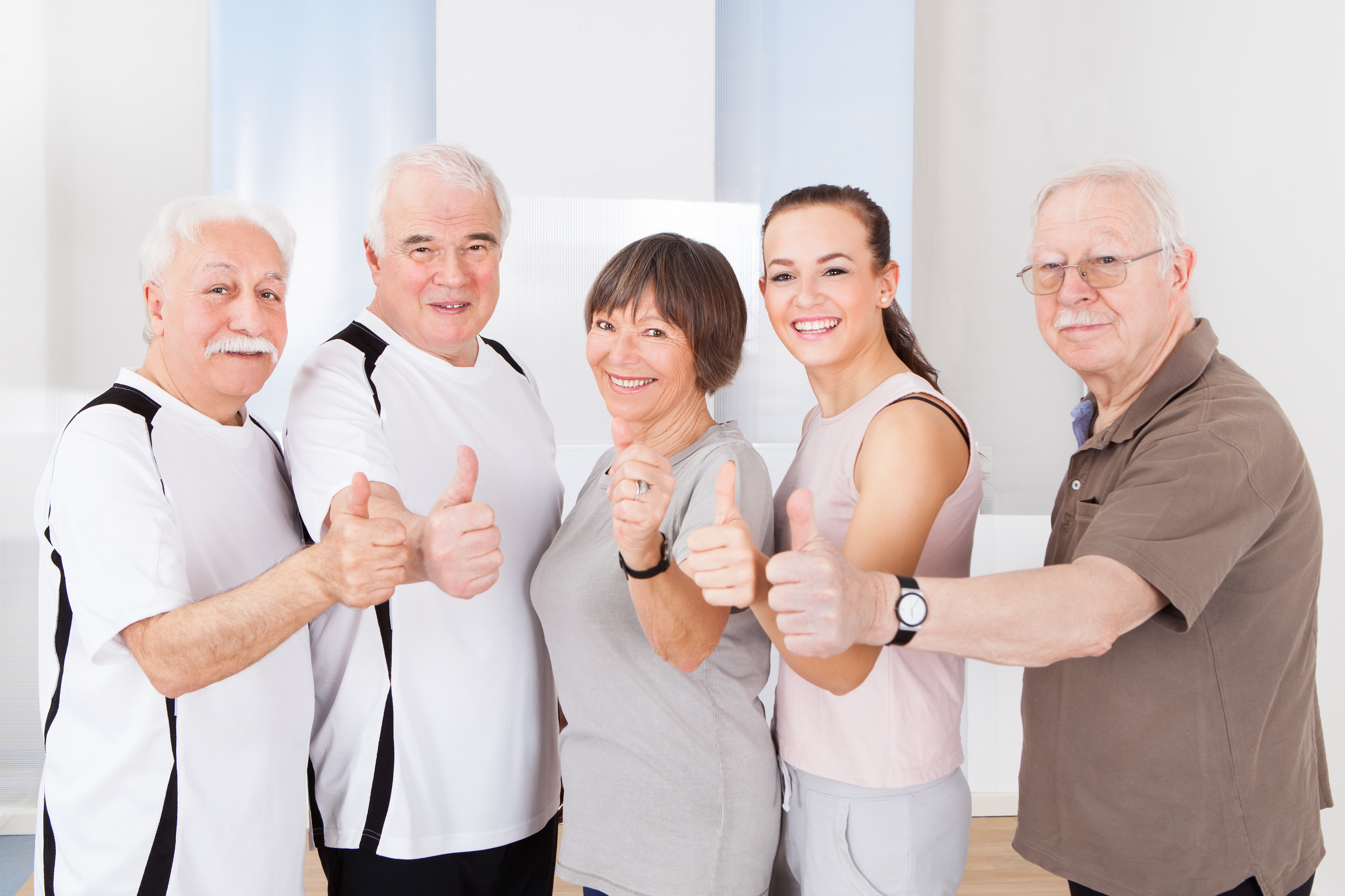 Portrait of confident trainer and senior customers showing thumbs up at healthclub